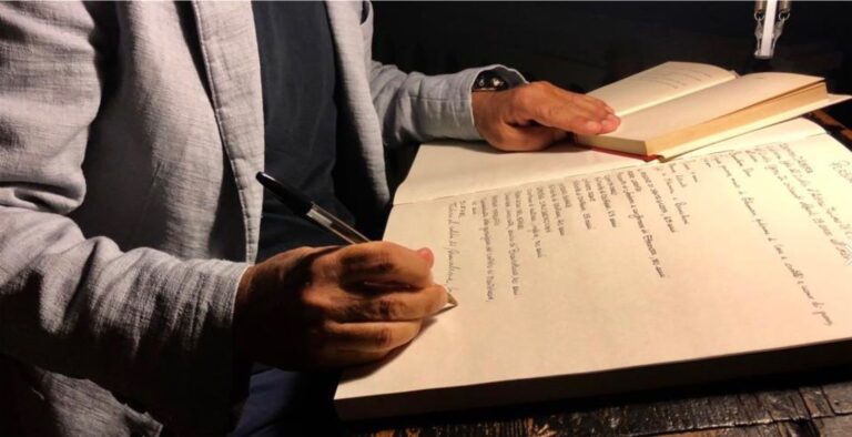 un uomo trascrive a mano un testo su un grande libro dalle pagine vuote, che man mano vengono riempite