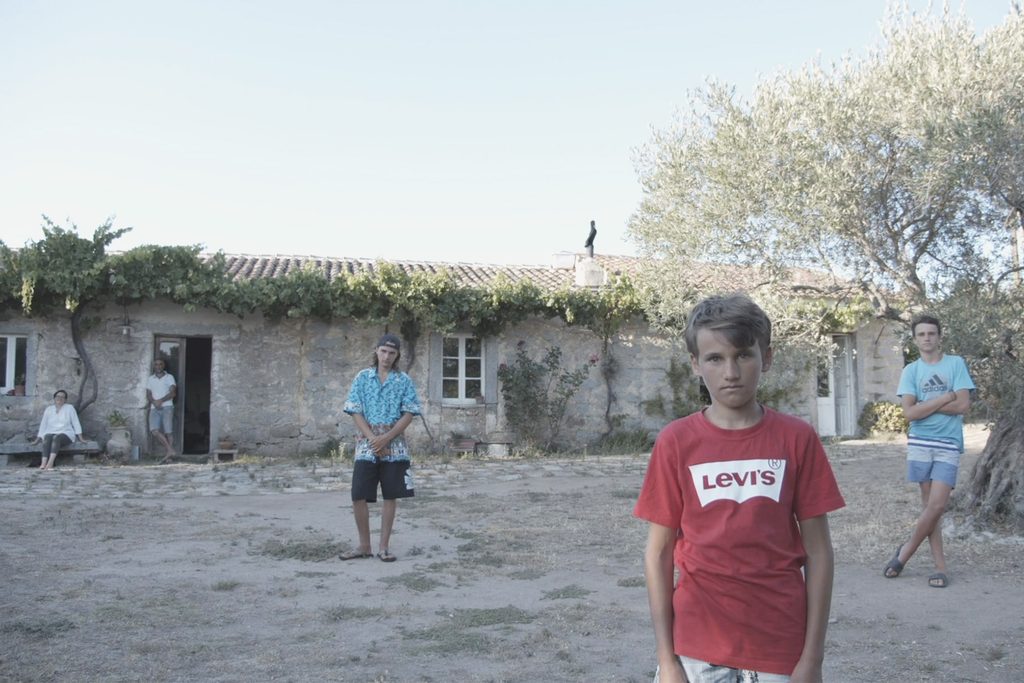 ritratto di una famiglia davanti a uno stazzo della gallura, con tre giovani ragazzi disposti a distanza tra di loro e i genitori sullo sfondo vicino all'uscio di casa